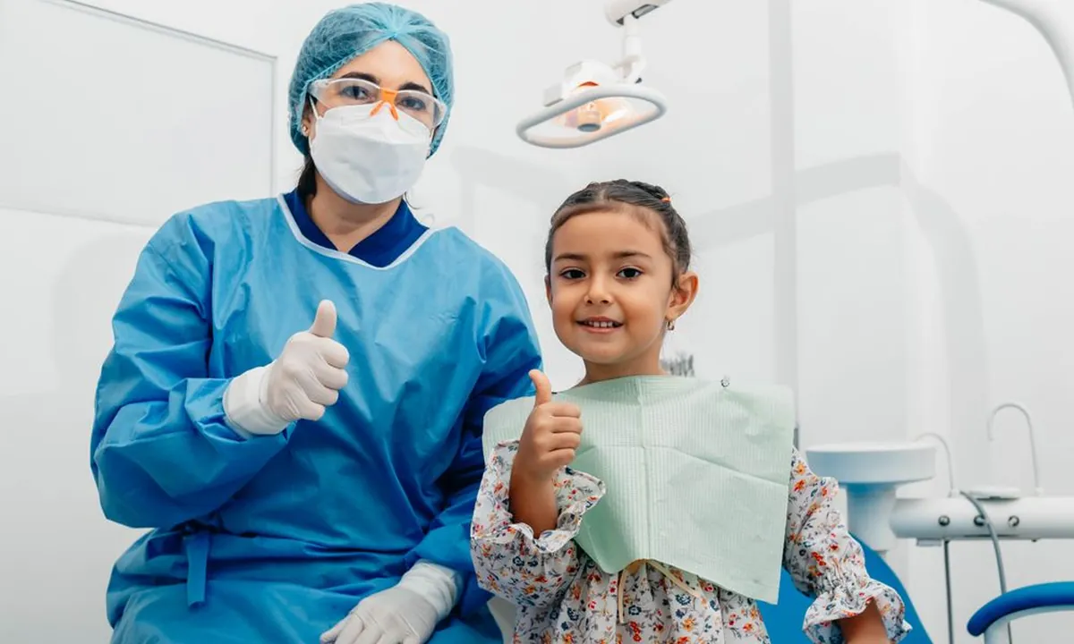 Diş hekimi ve küçük kızın başparmak yukarı işaretiyle gülümsemesi