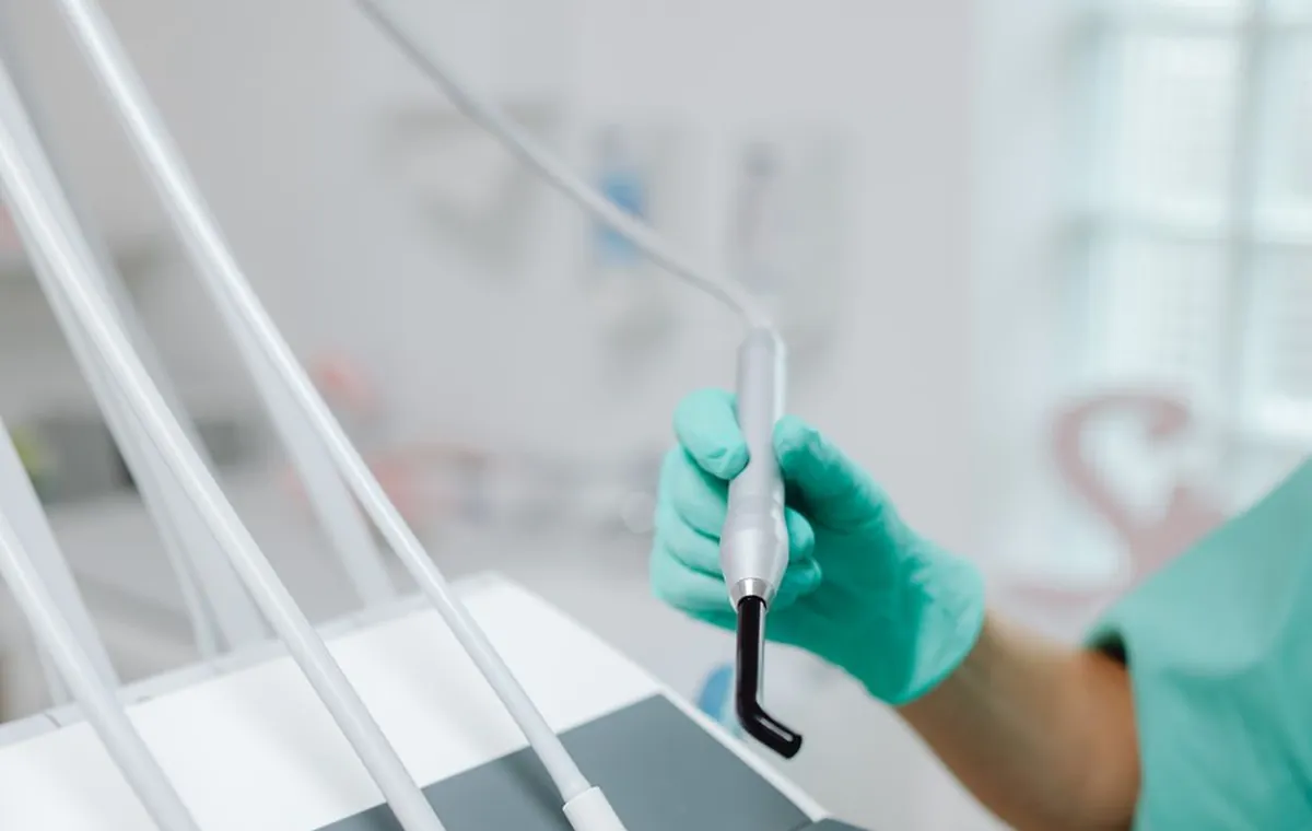 Diş kliniğinde steril paketli aletler ve hava-su spreyi tutan hekim eli